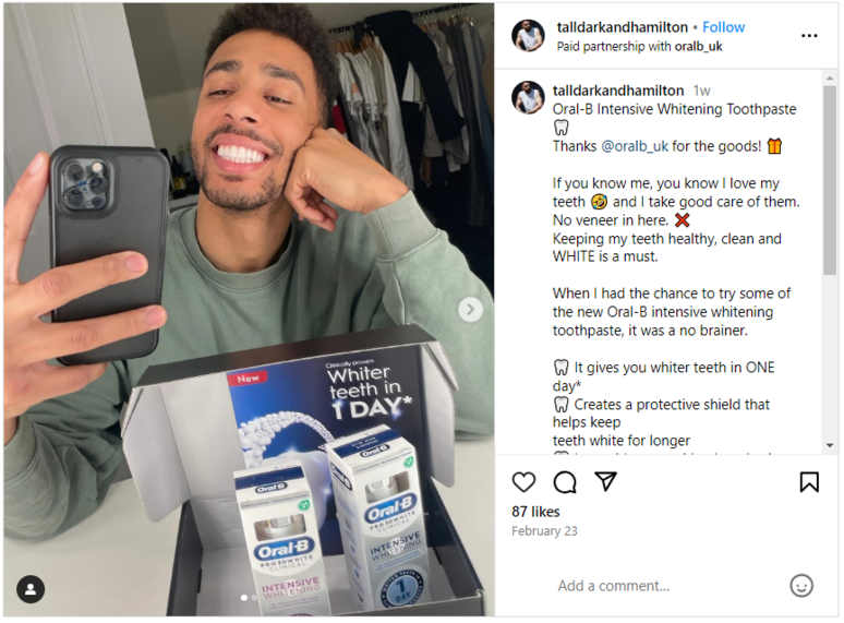 A man taking a mirror selfie while smiling and Oral-B tubes in the foreground